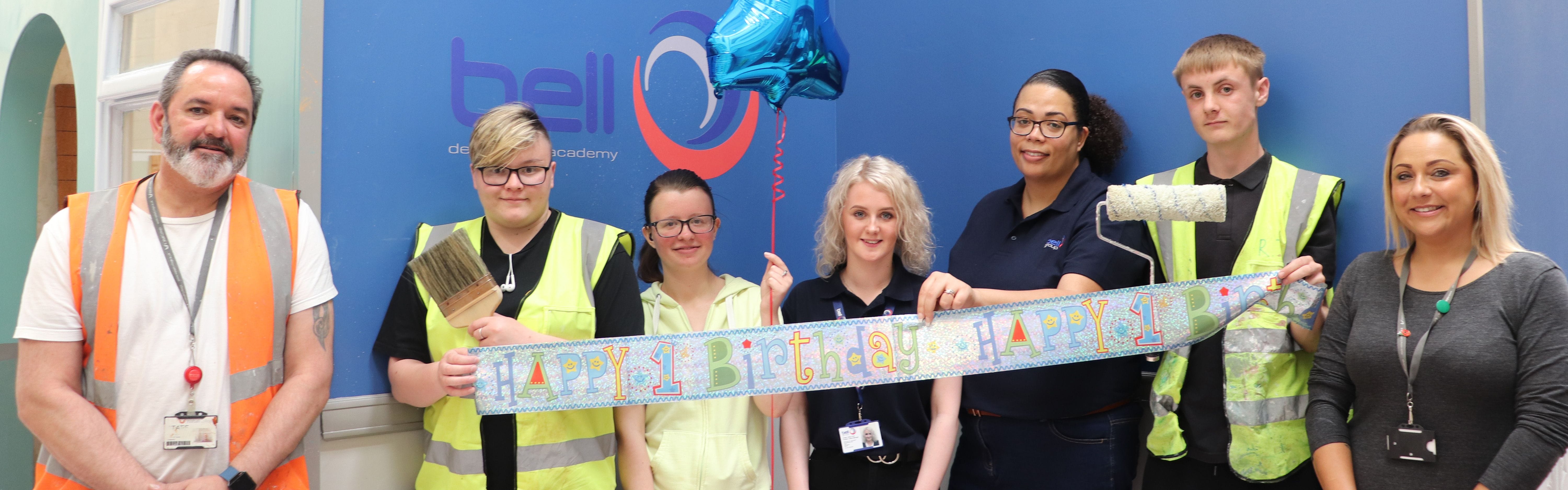 students, staff and Bell Academy representatives pose with first birthday banner facing