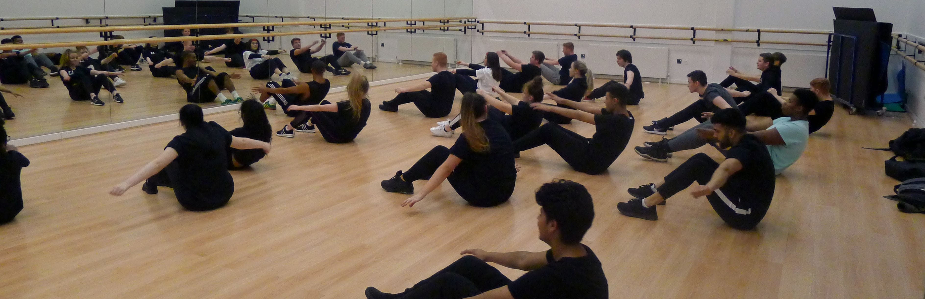 performing arts students sitting on studio floor with backs to camera