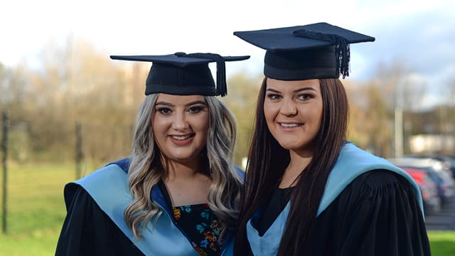two HE students in cap and gown