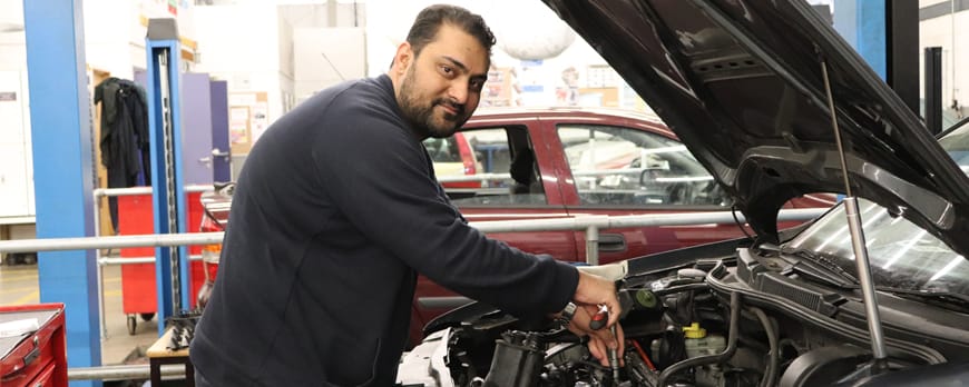 male adult learner lifts car bonnet and carries out vehicle maintenance facing