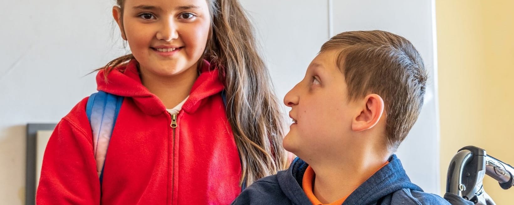 young female stands next to boy in wheelchair