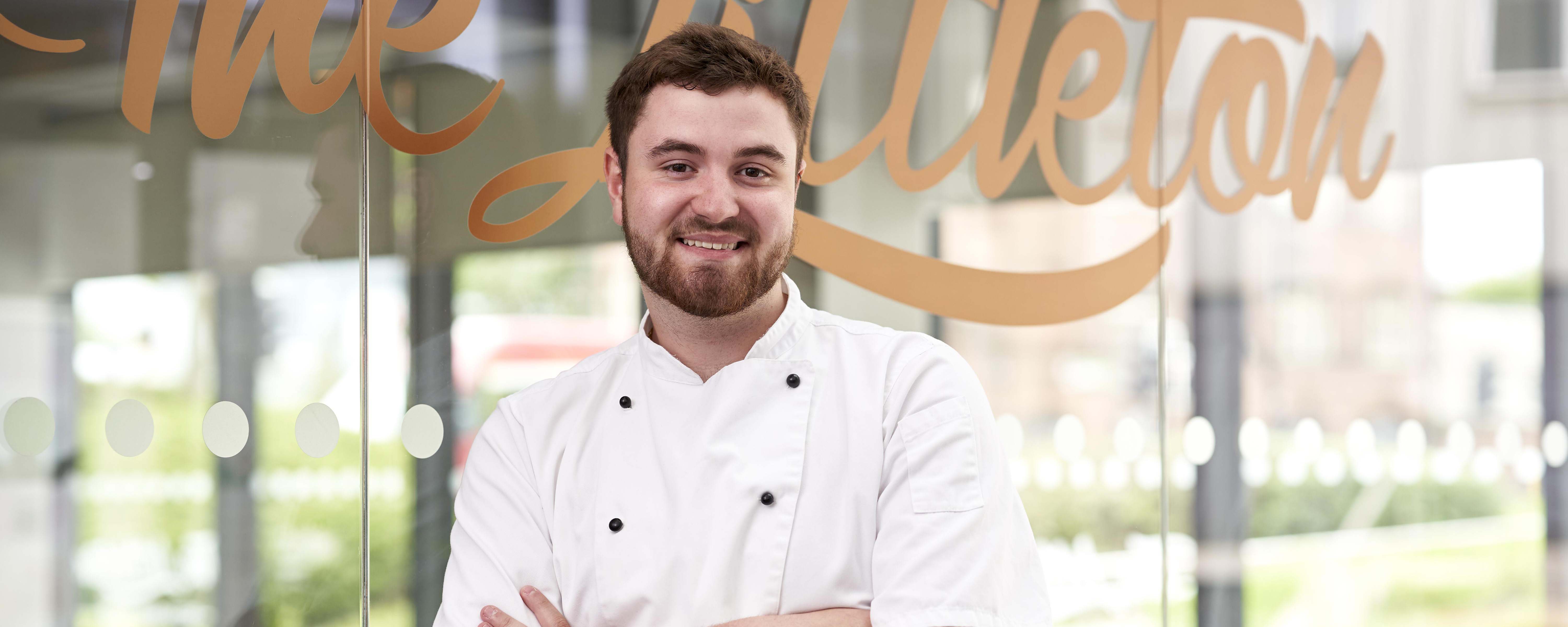 male chef standing in front of TheLittleton restaurant facing