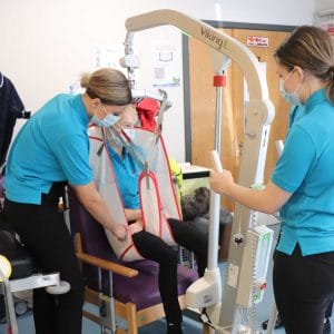 two female students assist mock patient using chair lift pulley