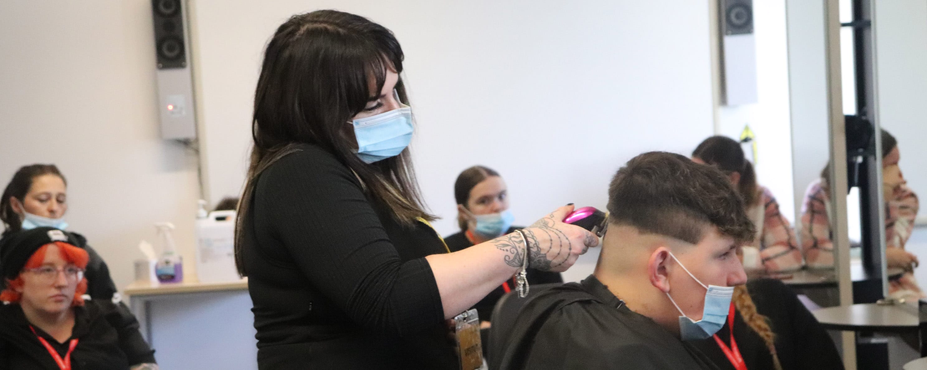 guest employer demonstrates barbering techniques on model watched by students