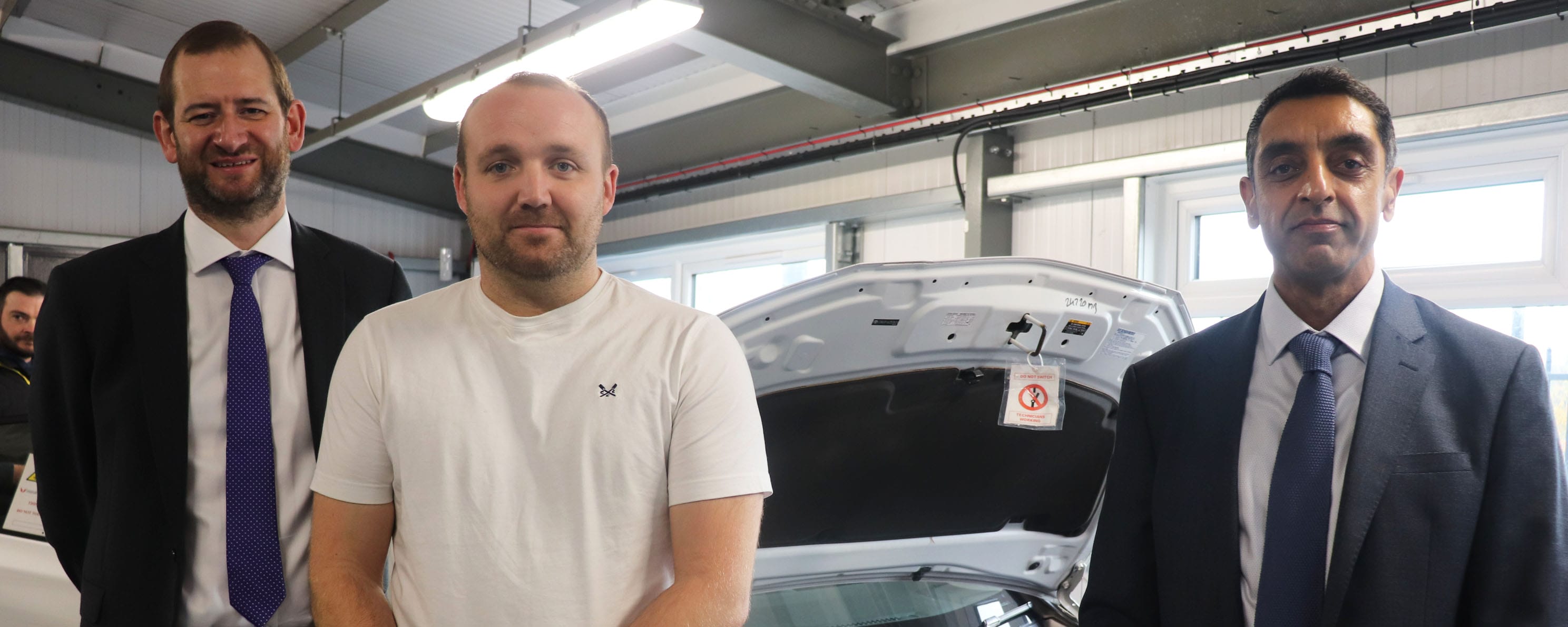 Department for Education representative with principal and student in electrical vehicle workshop facing