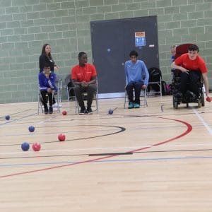 boccia player in wheelchair prepares to bowl watched by fellow competitors