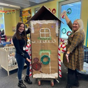 early years staff pose with gingerbread house in nursery classroom
