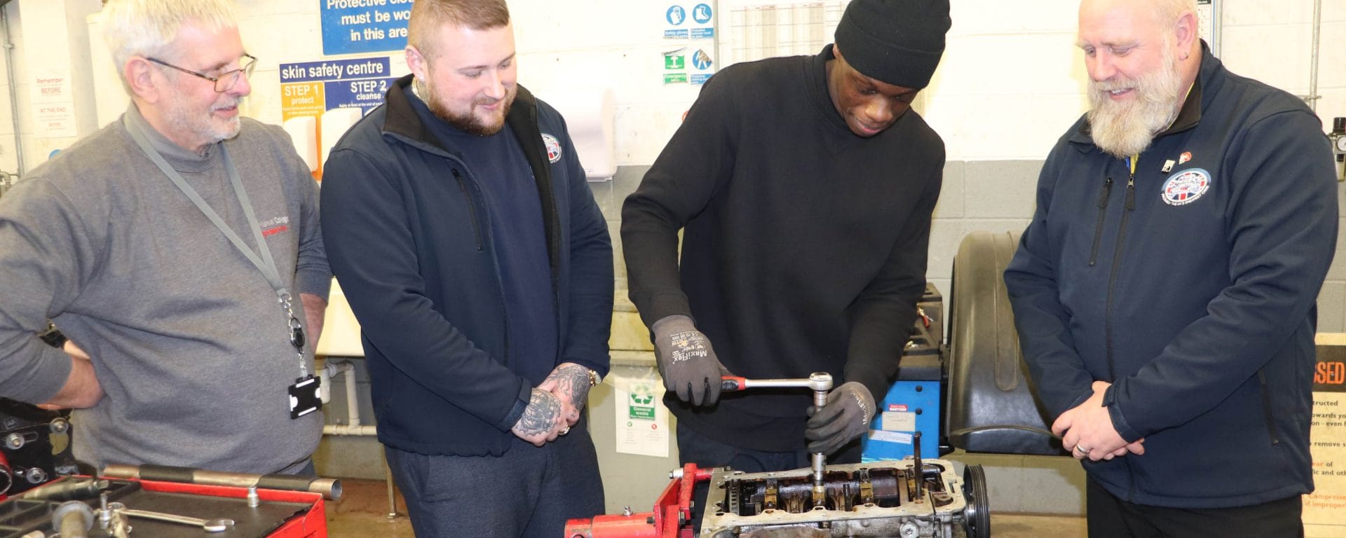 Trade Centre UK representatives and lecturer observe student working on an engine