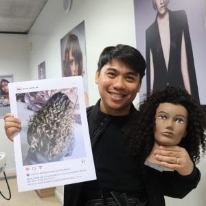 male student hairdresser holding instagram post screenshot and mannequin prize