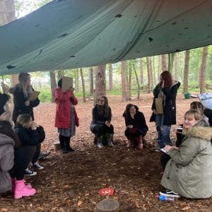 students sitting under outdoor Forest School den