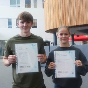 male and female student hold up their results slips facing
