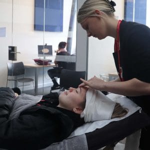 freshers fair attendee lying down on bed while receiving head massage from beauty student