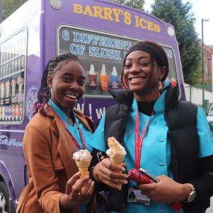 two female students pose with ice cream in front of van facing