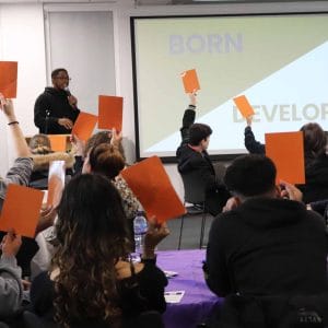 audience holding up cards while male guest speaker addresses them