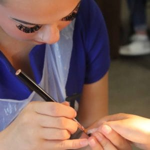 female student nail technician applies brush to nail of a client