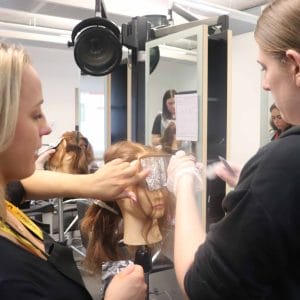 female hairdresser interacts female student colouring model's hair