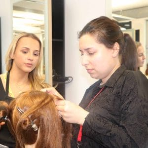 female hairdresser observes female student colouring model's hair