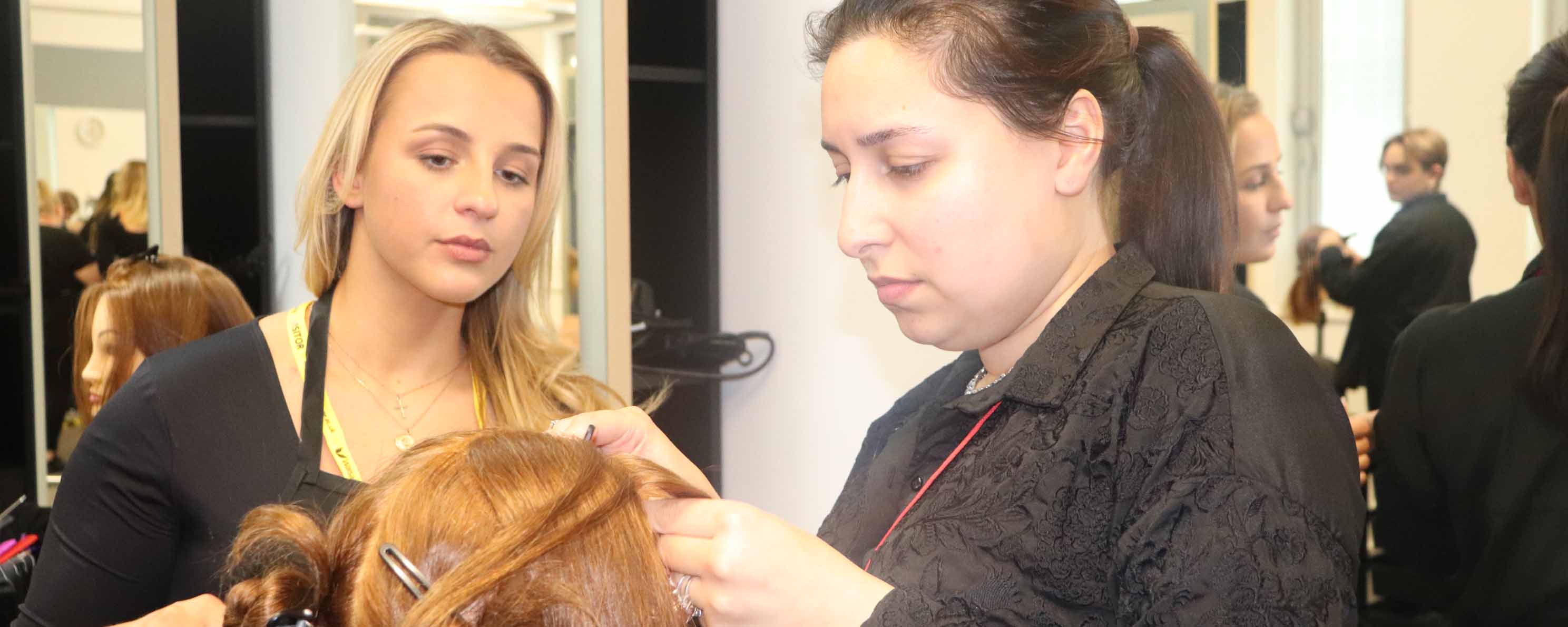 student hairdresser adjusts mannequin head hair watched by employer