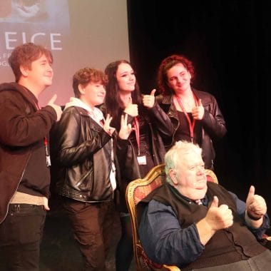 four students standing pose for photograph behind seated actor