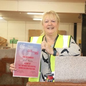 female lecturer poses against brickwork with certificate award facing