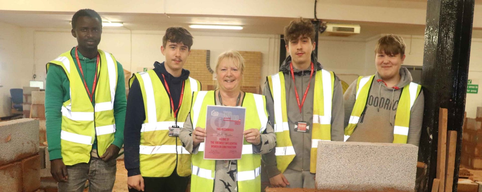 female lecturer poses with certificate next to students facing