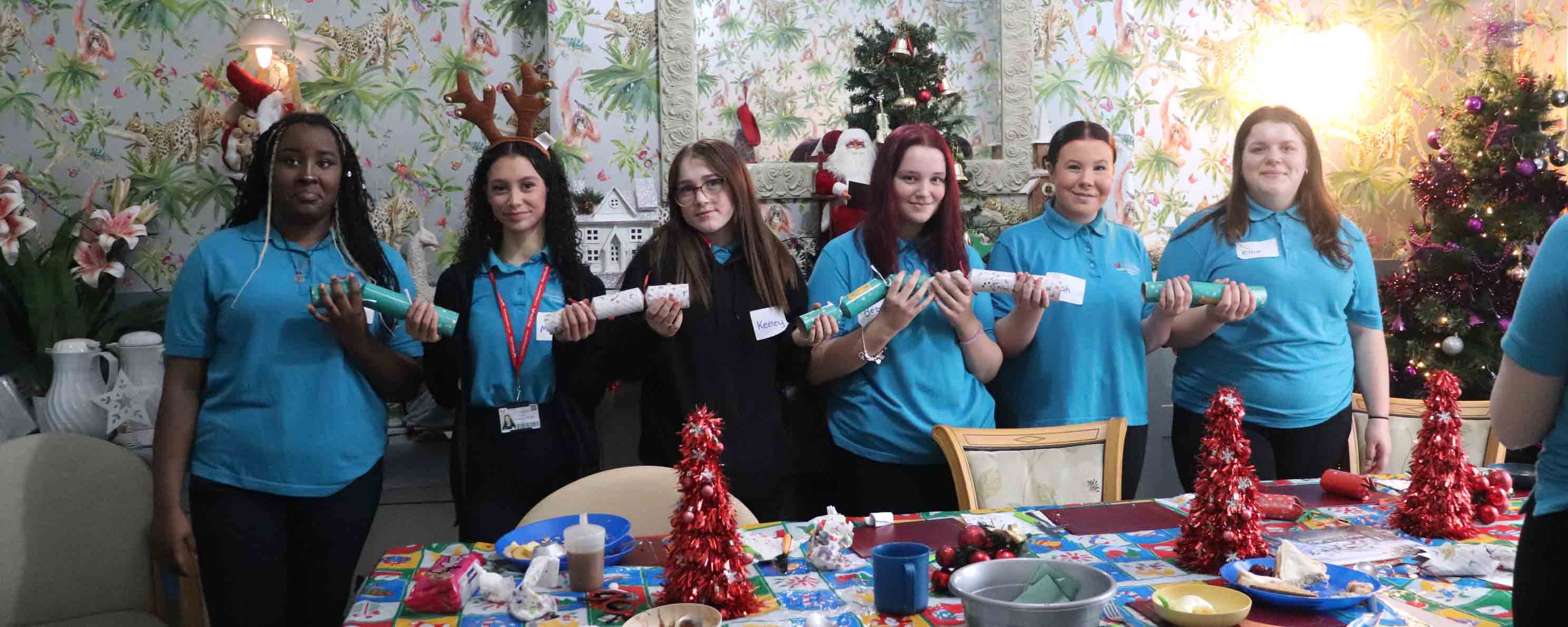 Students holding christmas crackers in front of a christmas tree