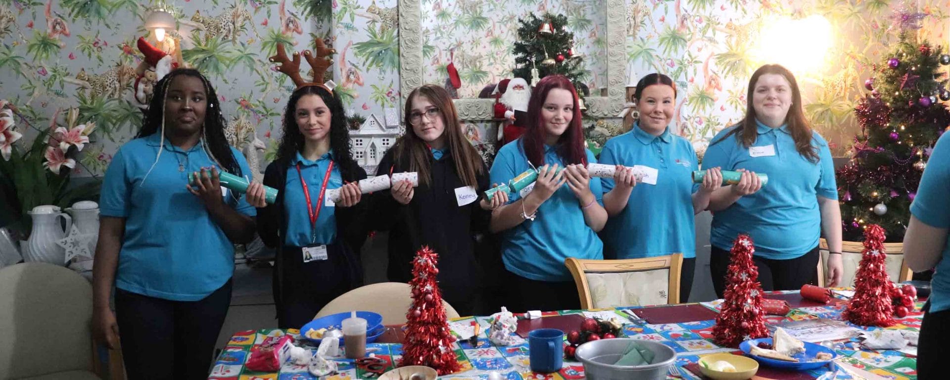 Students holding christmas crackers in front of a christmas tree