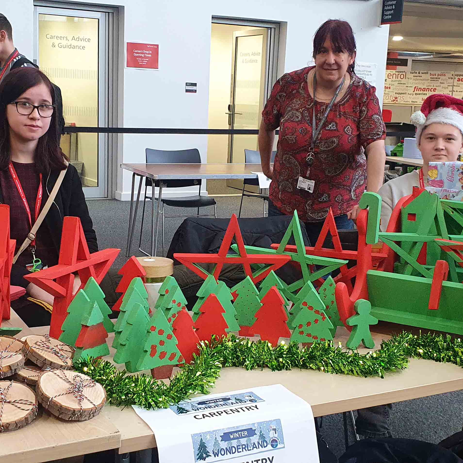 female students and lecturer seated at table selling ornaments facing