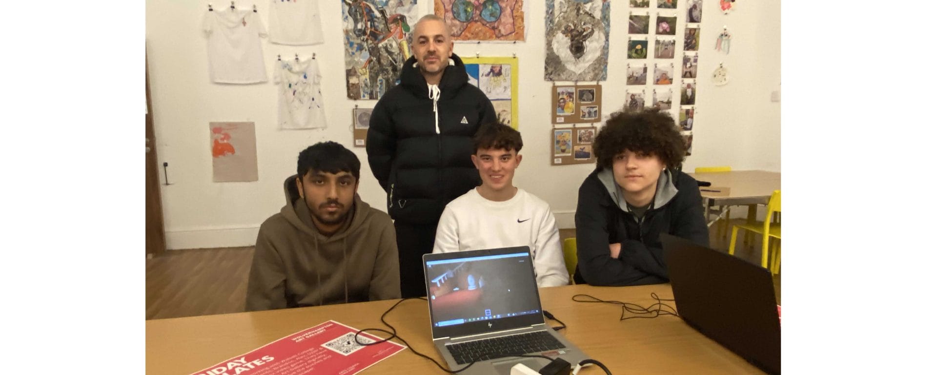 male computing students and art gallery representative faceing and seated with laptop showing Roblox game
