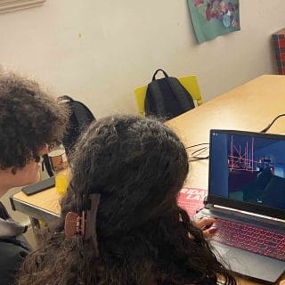 student demonstrates video game on laptop to guest visitor