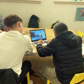 student demonstrates video game on laptop to guest visitor