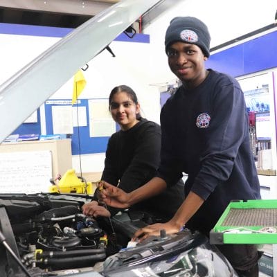 male and female student working on car engine facing