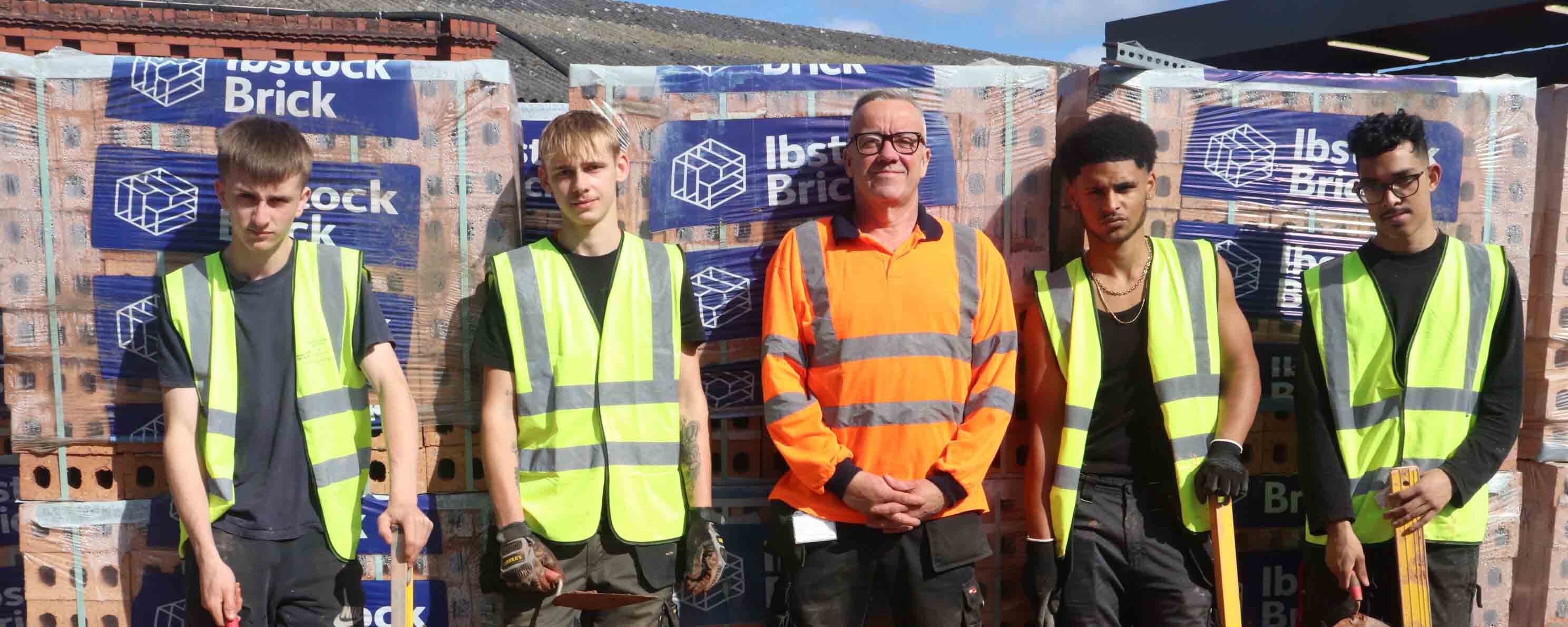 students and lecturer standing in front of bricks facing