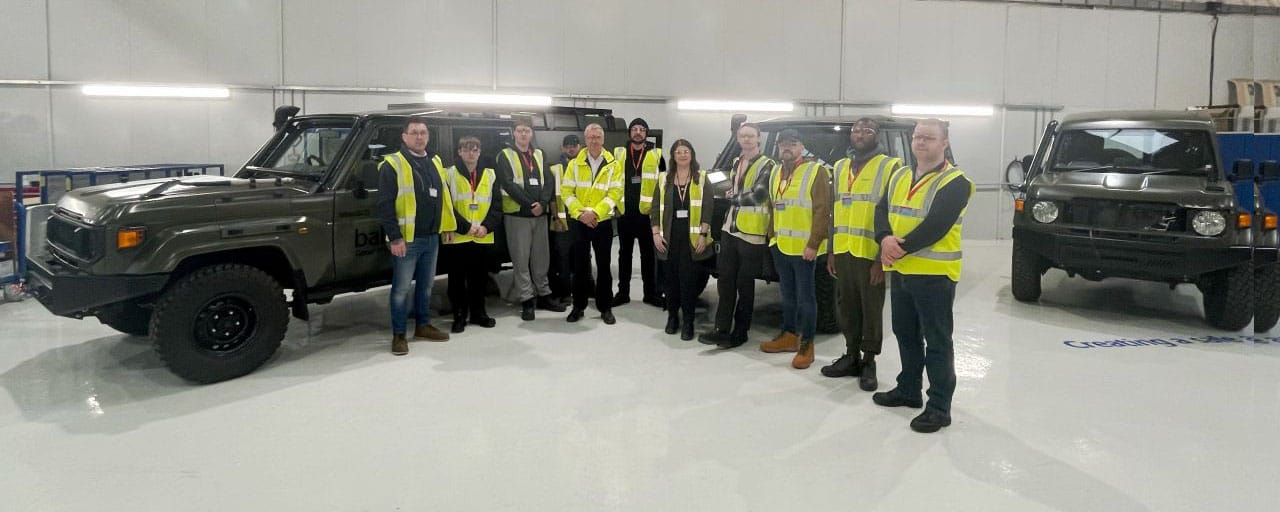 group of people on shop floor in front of vehicle facing