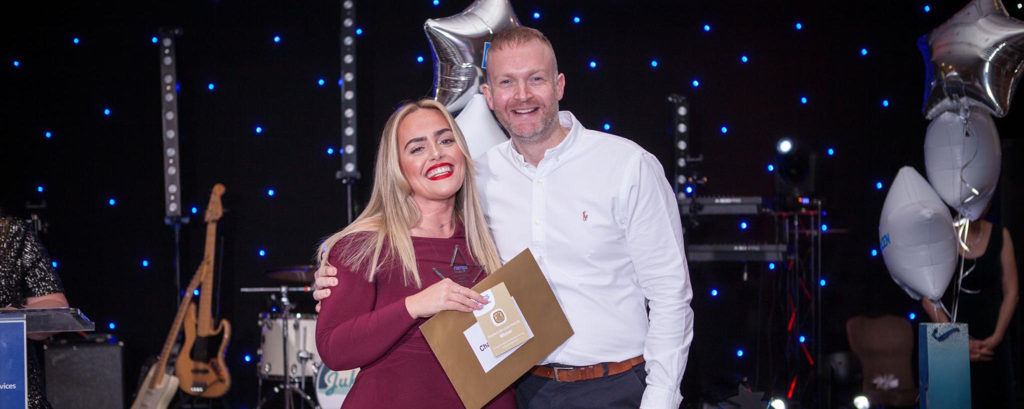 male award presenter with female award winner against stage backdrop
