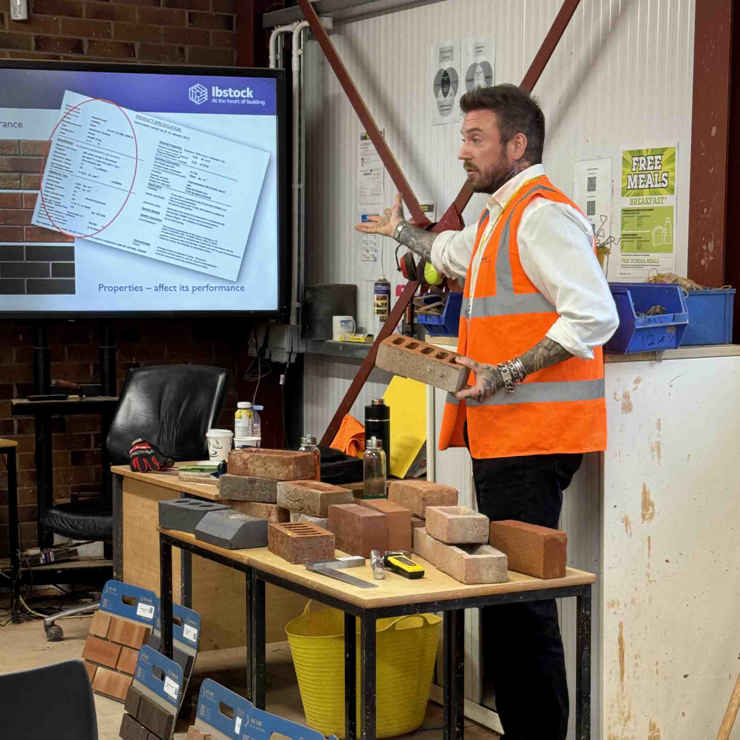male employer behind table with bricks addresses students