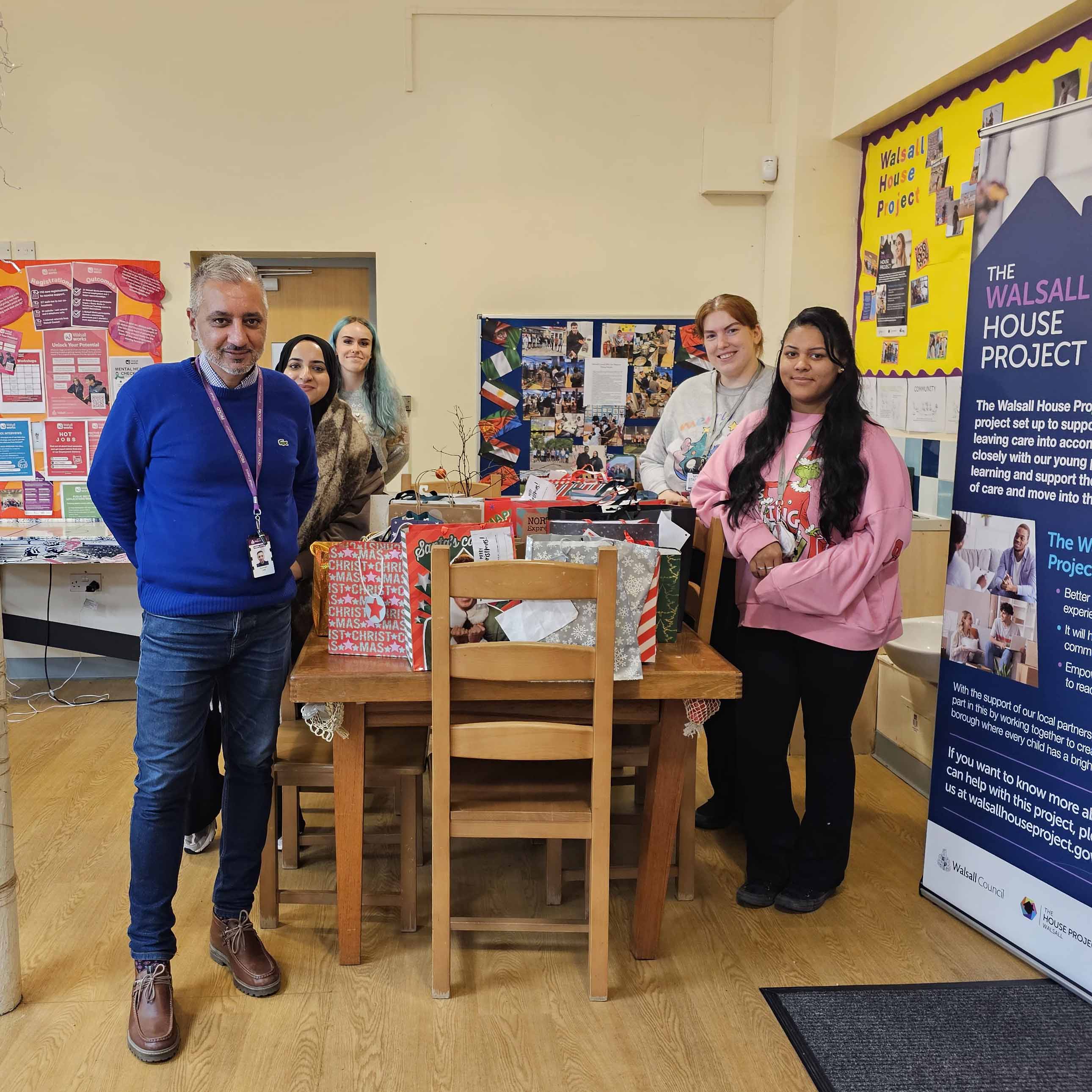 four people posing by table of donated gifts