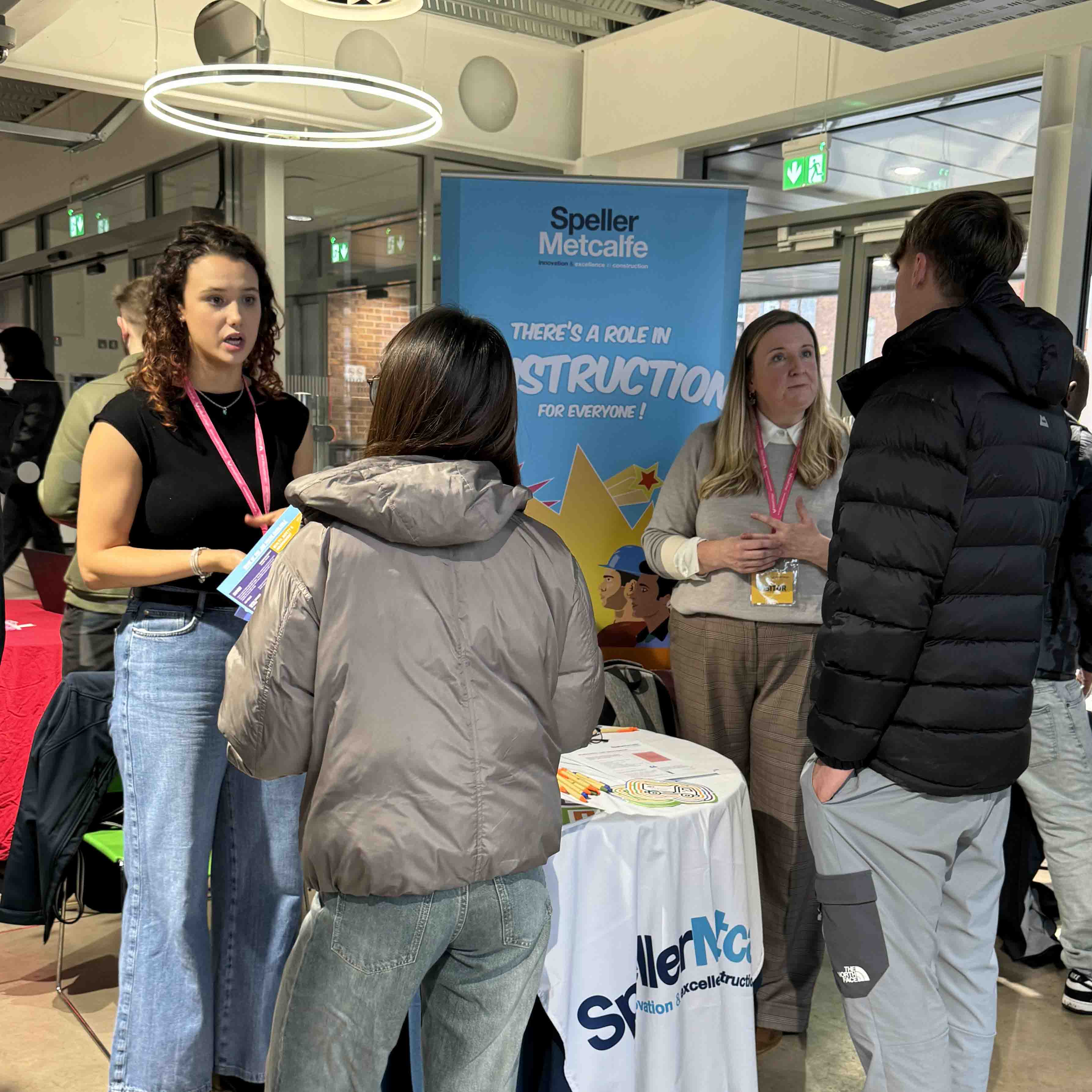 two female employers at exhibition stand speaking to a male and female student